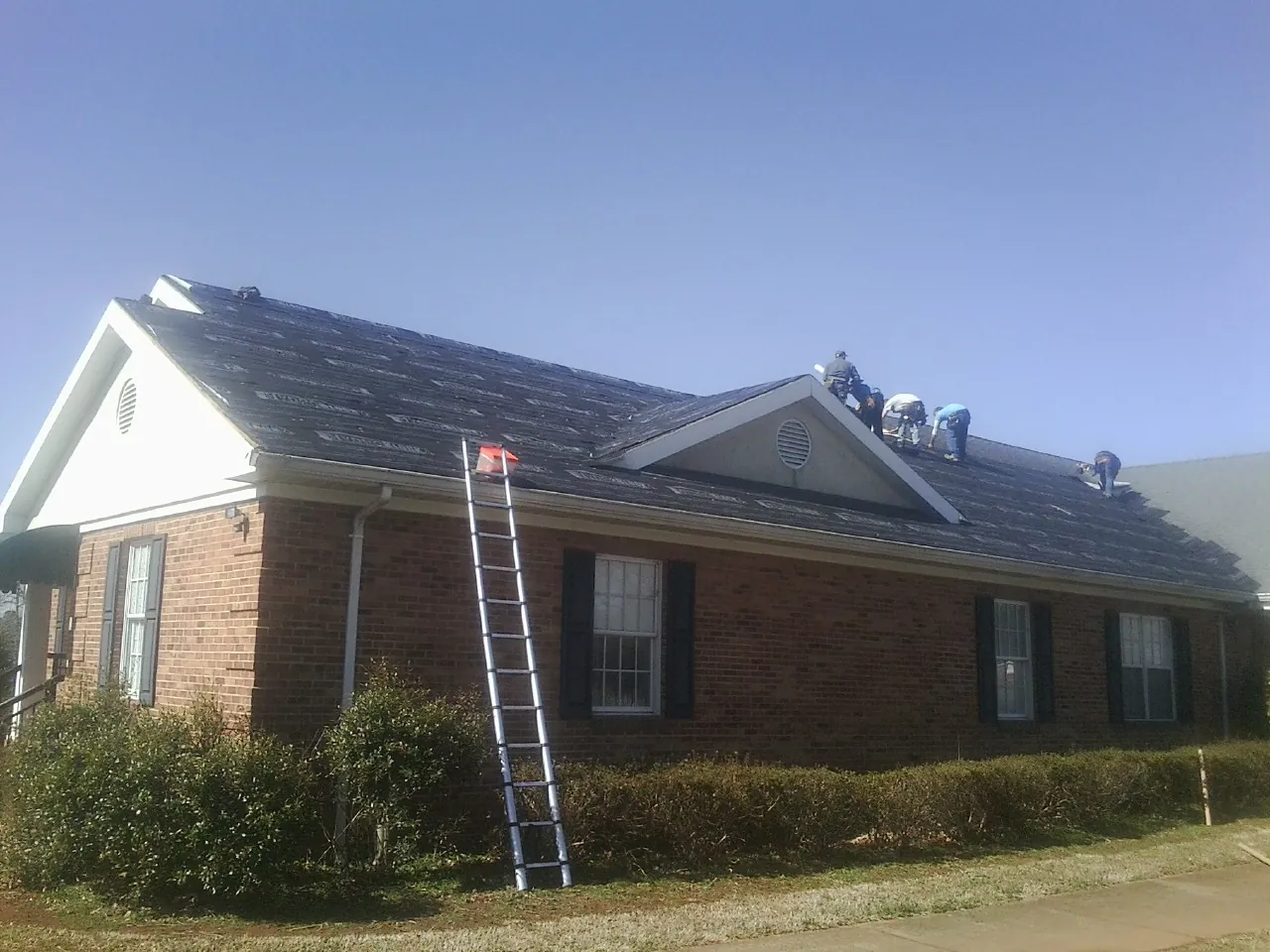Crew tearing shingles off a brick ranch roof with a ladder set — Metal Roof Repair work by our crew in Ruskin