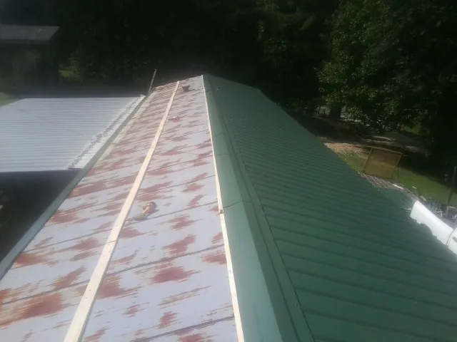 Old rusted panels beside newly installed green metal roofing — Wind Damage Roof Repair by Roofing Brothers in Ruskin