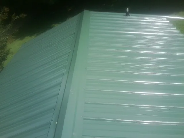 New green metal panels meeting at the ridge of a roof — Flat Roof Repair work by our crew in Ruskin